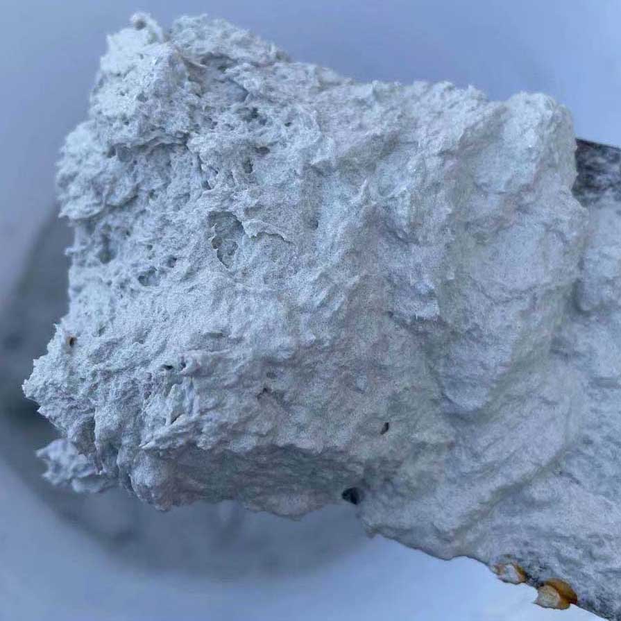 A close-up view of a grey, fibrous aerogel insulation coating with a rough, porous texture, held on a tool or spatula. The material appears lightweight and foamy, likely used for thermal insulation applications.