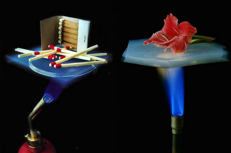 Two side-by-side images demonstrate the heat insulation properties of a transparent, lightweight material. On the left, a piece of aerogel is placed above a lit blowtorch, with wooden matches and a matchbox resting on top, remaining unburned. On the right, a red flower sits on a similar aerogel sheet above another lit blowtorch, staying intact despite the intense heat below.